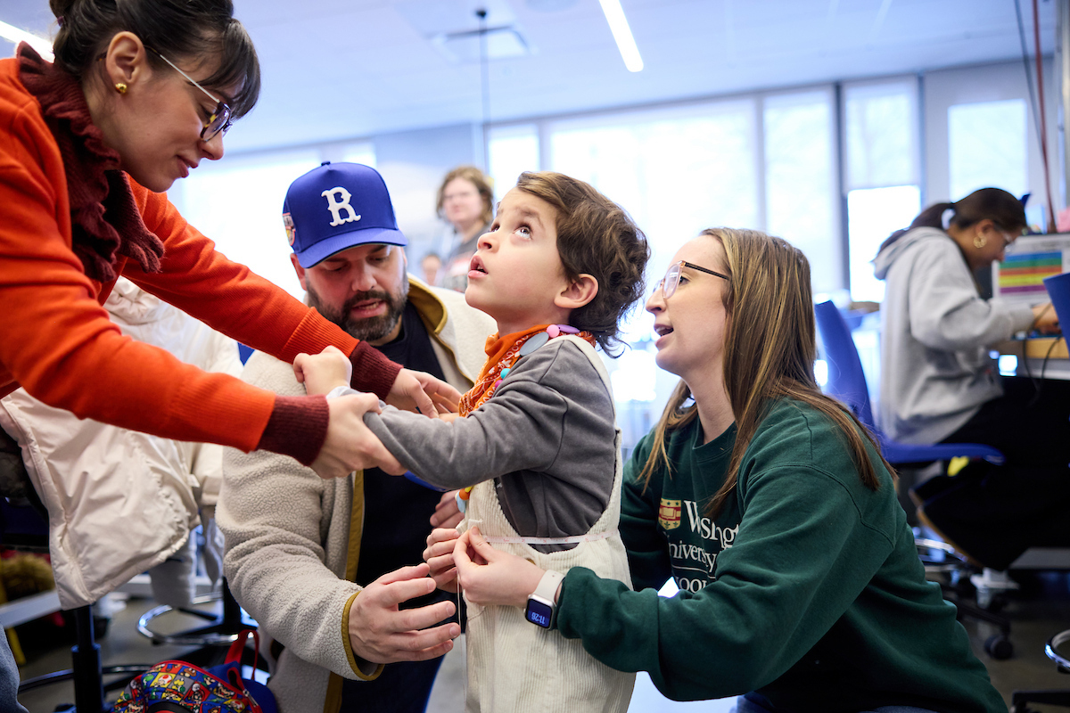 Dala and Jorge Rosado (left and second from left), help their son, Mateo, 4, get fitted for a wearable waterproof speaker vest at the McKelvey School of Engineering Spartan Light Metal Products Makerspace. The device will help Mateo simultaneously enjoy two things he loves: music and water. Brooke Anderson (right), a second-year occupational therapy graduate student at WashU Medicine, worked with three engineering students to design, test and build the product during the 2026 WashU Assistive Tech Make-a-Thon. (Credit: Matt Miller / WashU Medicine)